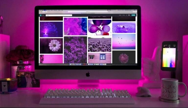 Modern desk setup with neon lighting and a desktop computer displaying colorful images.